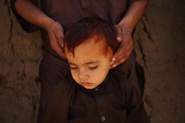 Caught in the middle of a firefight between Taliban fighters and the ANSF in Kapisa province, Jawad’s father blocks his son’s ears to dull the sound of gunfire, mortars and rocket-propelled grenades erupting around them, 2014 Andrew Quilty