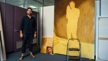 Christopher Bassi standing in an empty office next to a large yellow painting