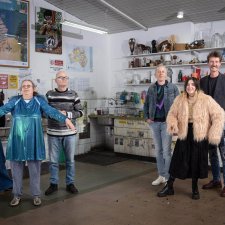 Two grounps of three people standing in a studio with walls and shelves filled with artworks