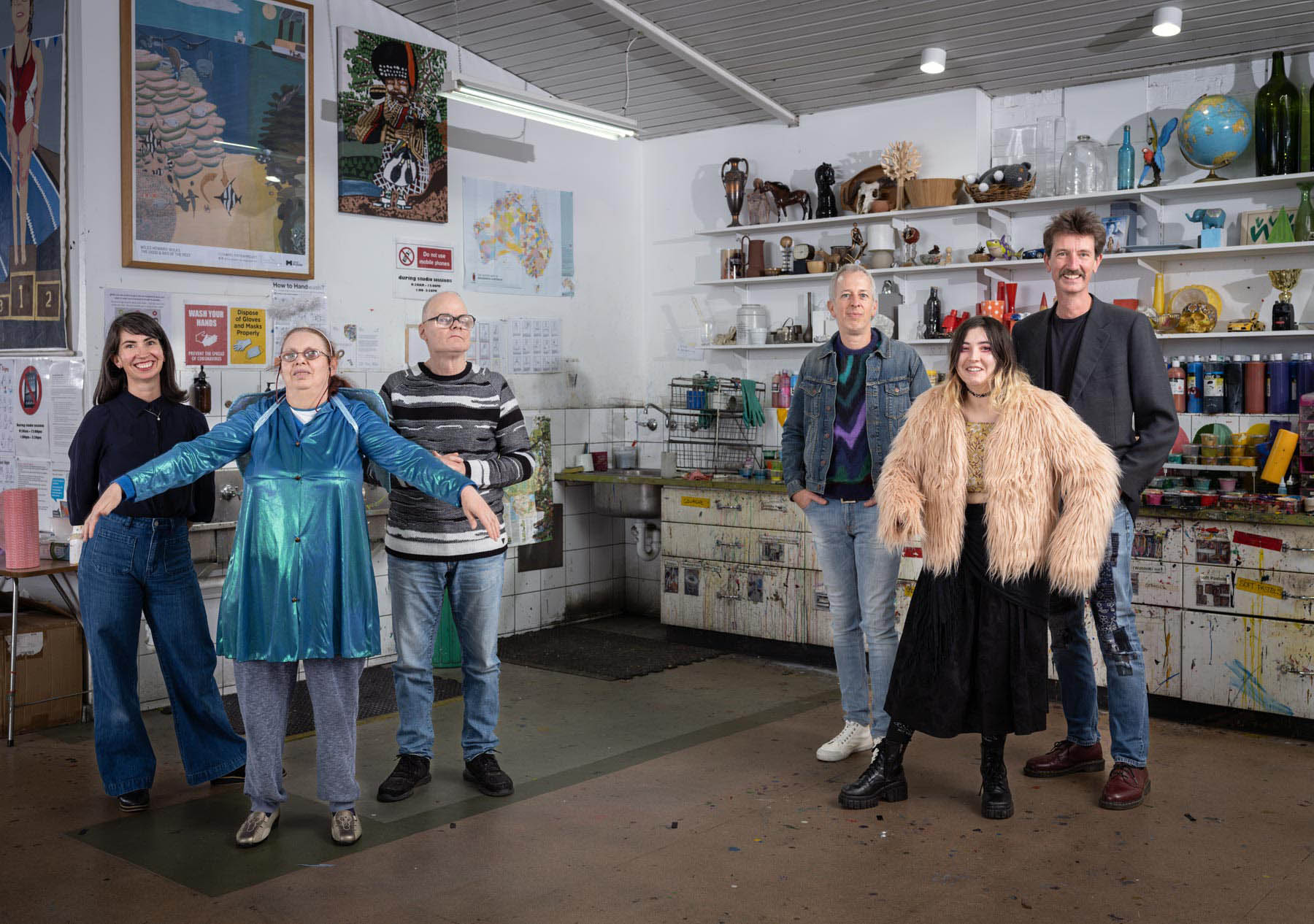 Two grounps of three people standing in a studio with walls and shelves filled with artworks