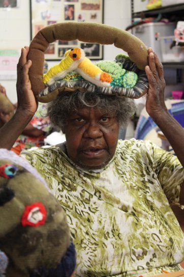 Yarrenyty Arltere Artist Marlene Rubuntja demonstrates the coolamon full of bush food that will be placed on her soft self portrait, 2022