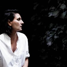 Angelica Mesiti in profile wearing a white linen shirt in front of a dark leafy hedge