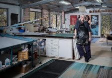 Alison Alder wearing a paint splattered apron, leaning against a bench in her studio