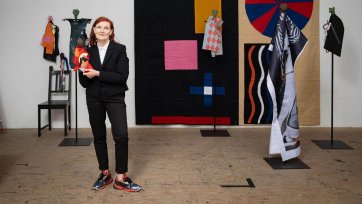 Sally Smart standing in her wooden floored studio holding a puppet