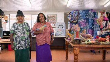 Dulcie Sharpe and Rhonda Sharpe in a room with a brown tile floor, next to a wooden table with soft animal sculptures