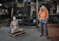 Nell standing in her workshop next to a cross legged sculpture