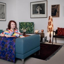 Deborah Kelly sitting on a blue couch in a room with artworks on the walls