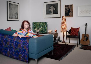 Deborah Kelly sitting on a blue couch in a room with artworks on the walls