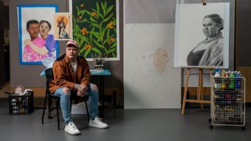 Dylan Mooney sitting on a chair in front of a wall with paintings and drawings